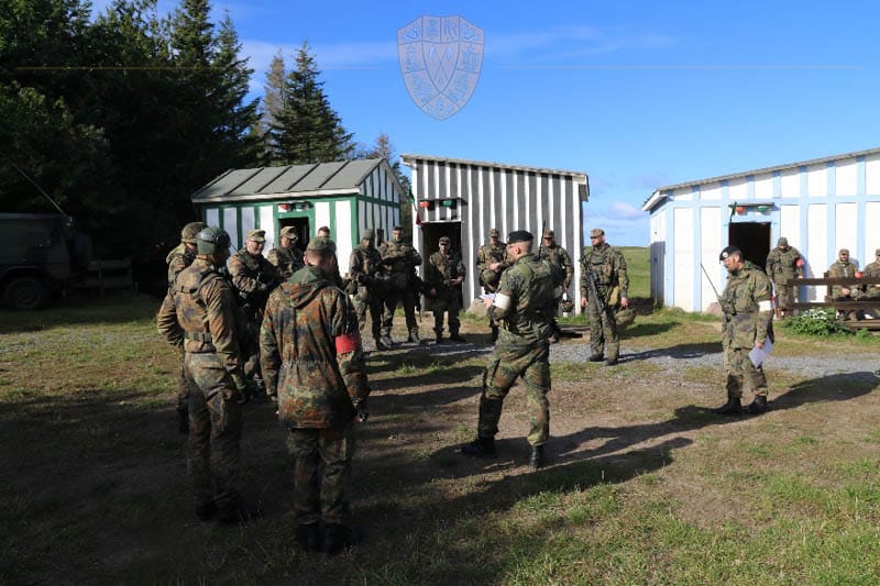 Soldaten stehen im Kreis. Im Hintergrund Bäume und die Schießanlage