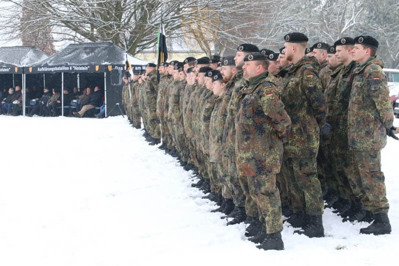 Soldaten sind angetreten auf dem Bataillonsrasen. Es liegt Schnee. Im Hintergrund sind Pagodenzelte mit den Gästen zu sehen.