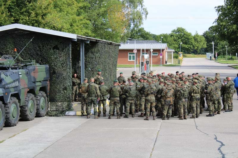 Viele Soldaten stehen im Halbkreis vor dem Brigadegeneral, der den Auftrag erklärt. Bundeswehr gelände, im Hintergrund das Wachgebäude mit der Kasernenzufahrt