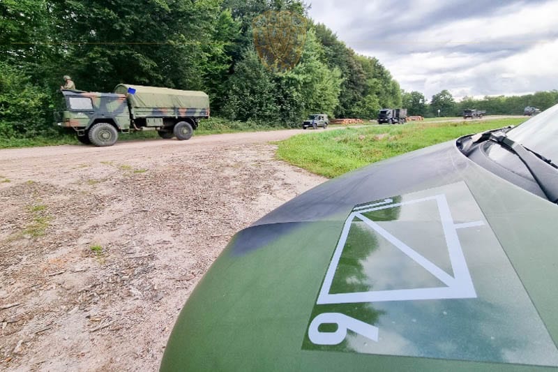 IM VORDERGRUND DIE MOTORHAUBE EINES PKW MIT TAKTISCHEN ZEICHEN. Im Hintergrund Militär LKW und Radpanzer